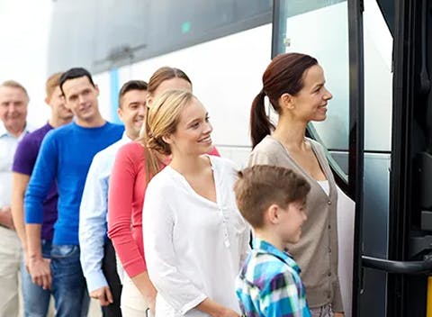 A line of diverse passengers, including men, women, and a child, smiling as they board a public bus.