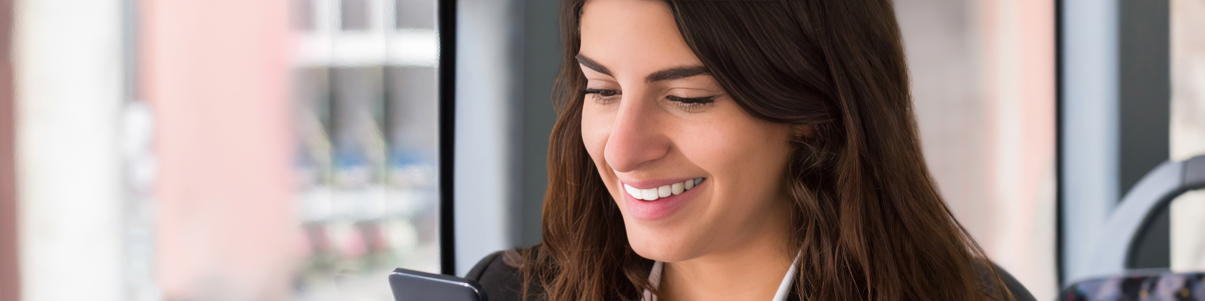 Smiling woman sitting on public transit looking at her smartphone, suggesting onboard Wi-Fi or mobile connectivity for a better passenger experience.