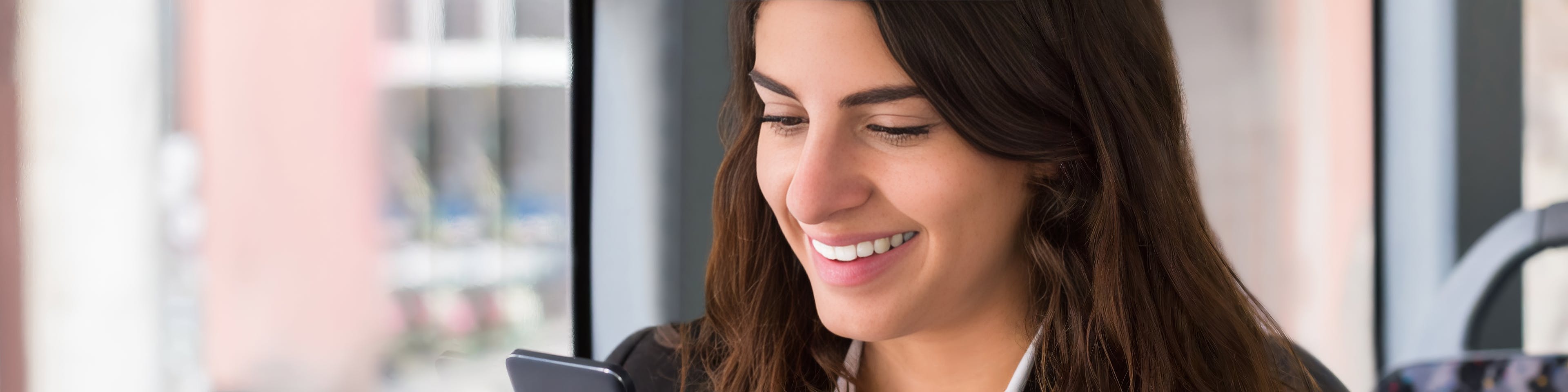 Smiling woman sitting on public transit looking at her smartphone, suggesting onboard Wi-Fi or mobile connectivity for a better passenger experience.