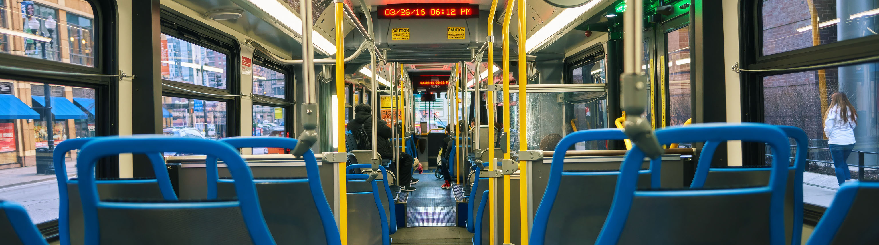 Interior view of a city bus with blue and yellow seats, featuring an overhead LED display.