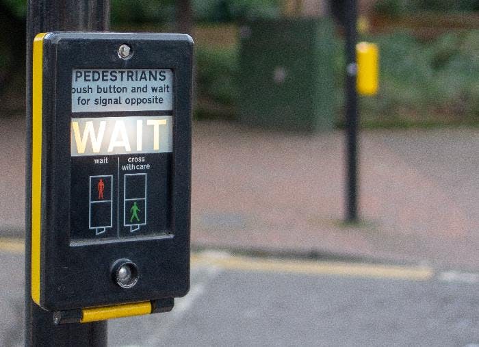 A UK pedestrian crossing button with the word WAIT illuminated, indicating that it is not safe for the pedestrian to cross