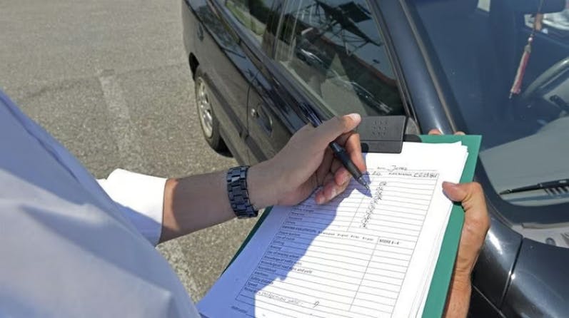 Photograph of a driving test examiner stood next to a car with a marksheet