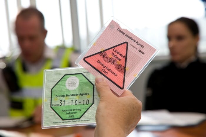 Photograph of a hand holding a Potential Driving Instructor (PDI) DVSA-issued badge and an Approved Driving Instructor (ADI) DVSA-issued badge