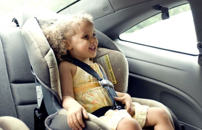 Photograph of a young girl sitting in a child's car seat in the back of a car