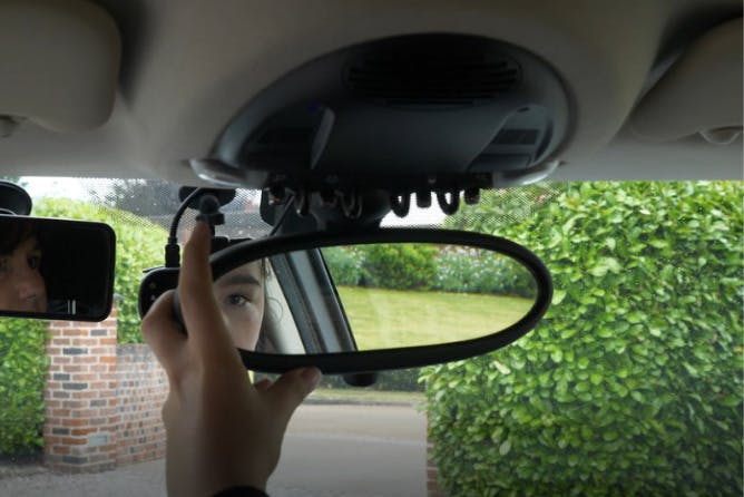An image of a person adjusting the rear view mirror in a car 