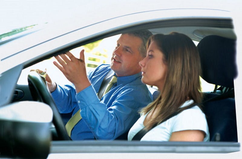 Driving instructor and learner driver sit in a car together while the instructor gives directions