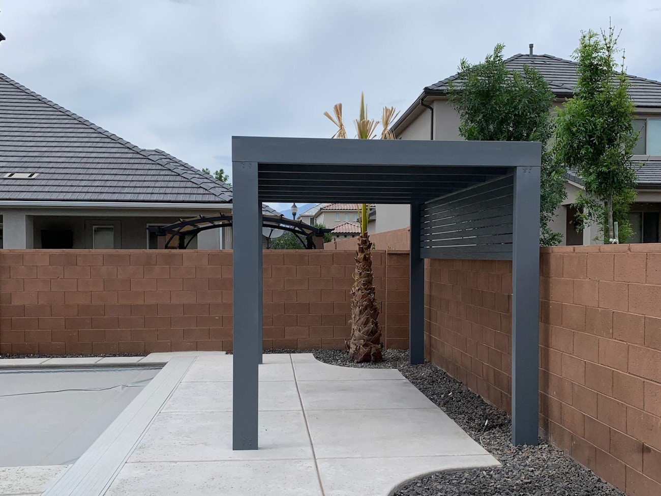Gray awning by poolside in Las Vegas backyard with a lattice privacy wall