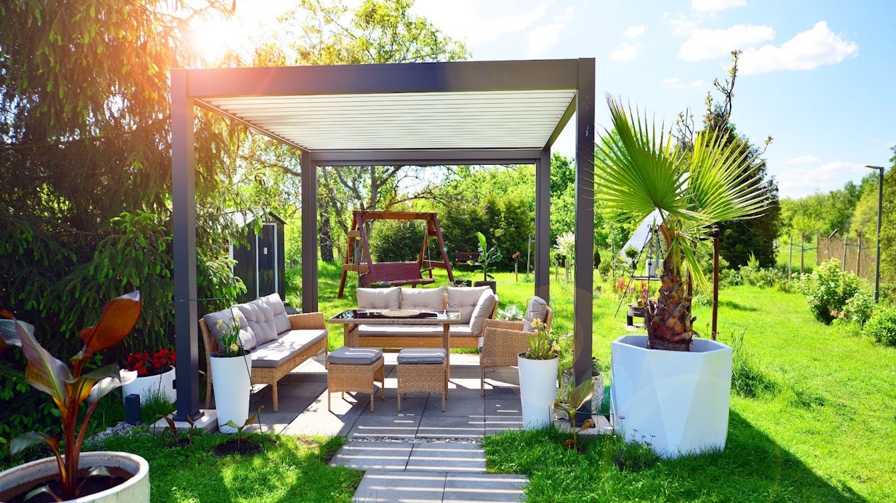 Modern aluminum patio cover ideas over an outdoor seating area surrounded by greenery, illustrating stylish and comfortable backyard design.