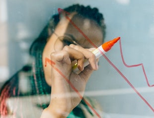 A photo that shows a woman drawing graphs on a glass board.