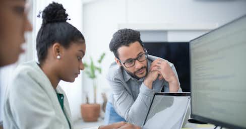 People in an office setting looking at a laptop.