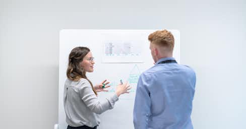 A woman and a man talking in front of a white board.