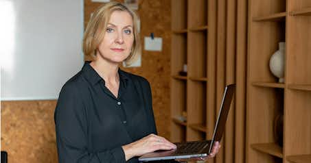 Woman in an office setting holding a laptop.