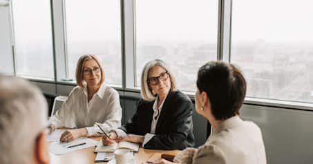 Three women and a man in a conference room in the middle of a work meeting.