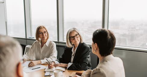 Three women and a man in a conference room in the middle of a work meeting.
