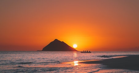 Image of a sunset with a mountain at the back and a kayak next to a beach.
