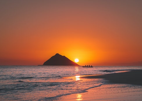 Image of a sunset with a mountain at the back and a kayak next to a beach.