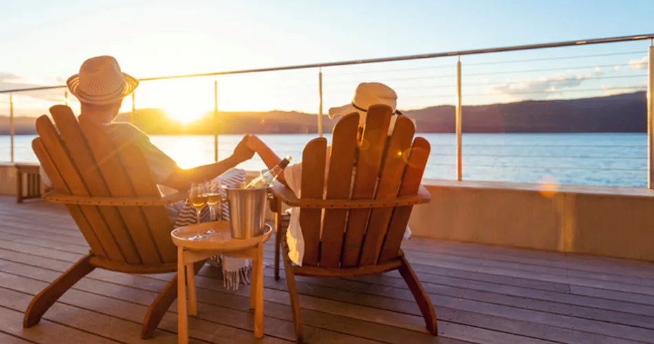 Couple sitting on beach chairs, holding hands during sunset