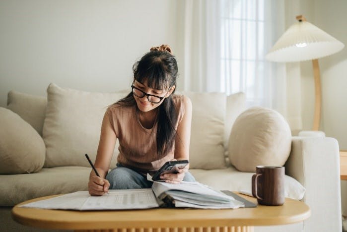 Young woman with glasses at a table in her apartment writing on financial documents