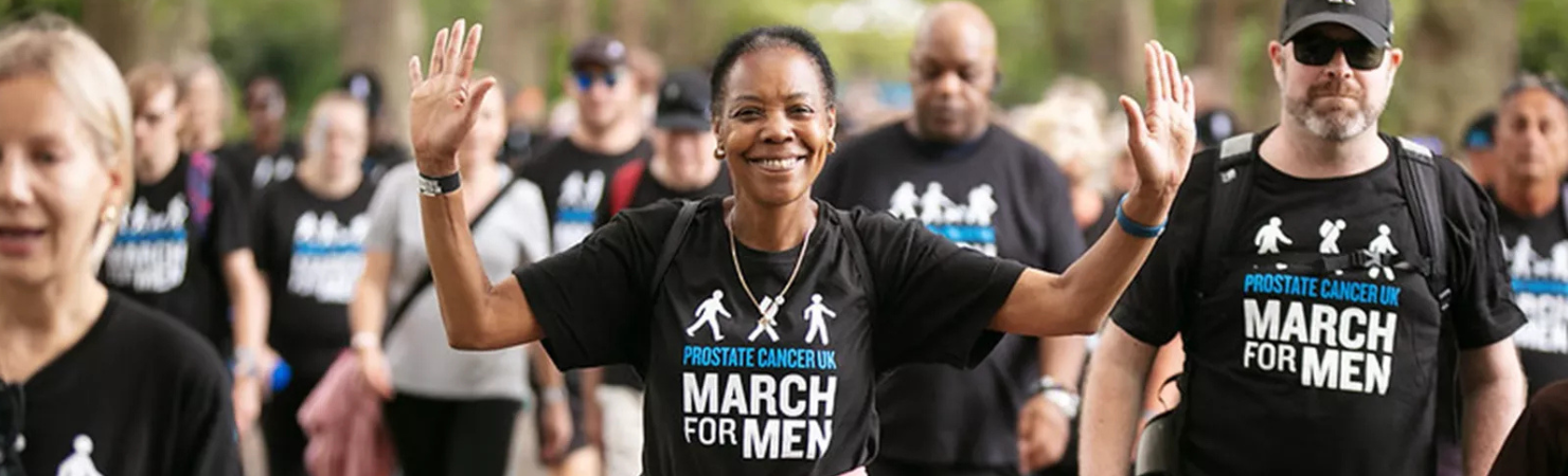 A lady with her arms up walking towards the camera wearing a March for Men t-shirt