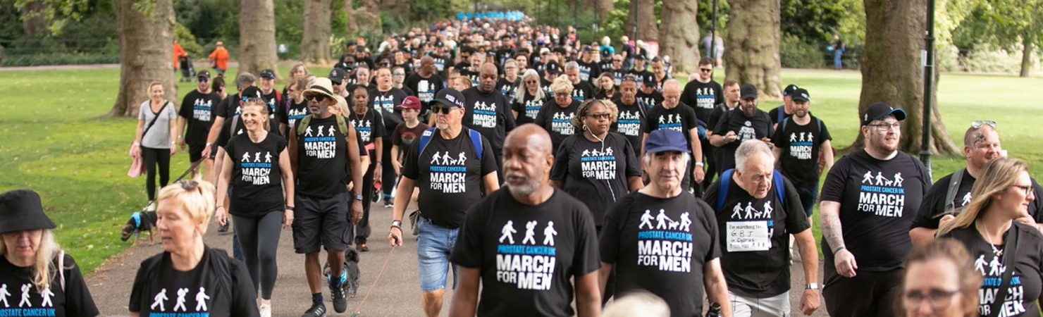 A big group of people walking in a park wearing Prostate Cancer UK March for Men t-shirts