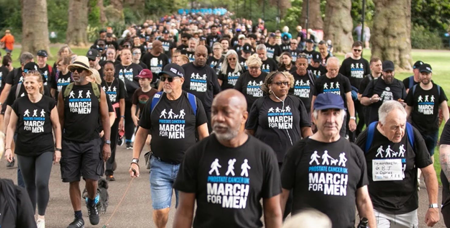 A big group of people walking in a park wearing Prostate Cancer UK March for Men t-shirts