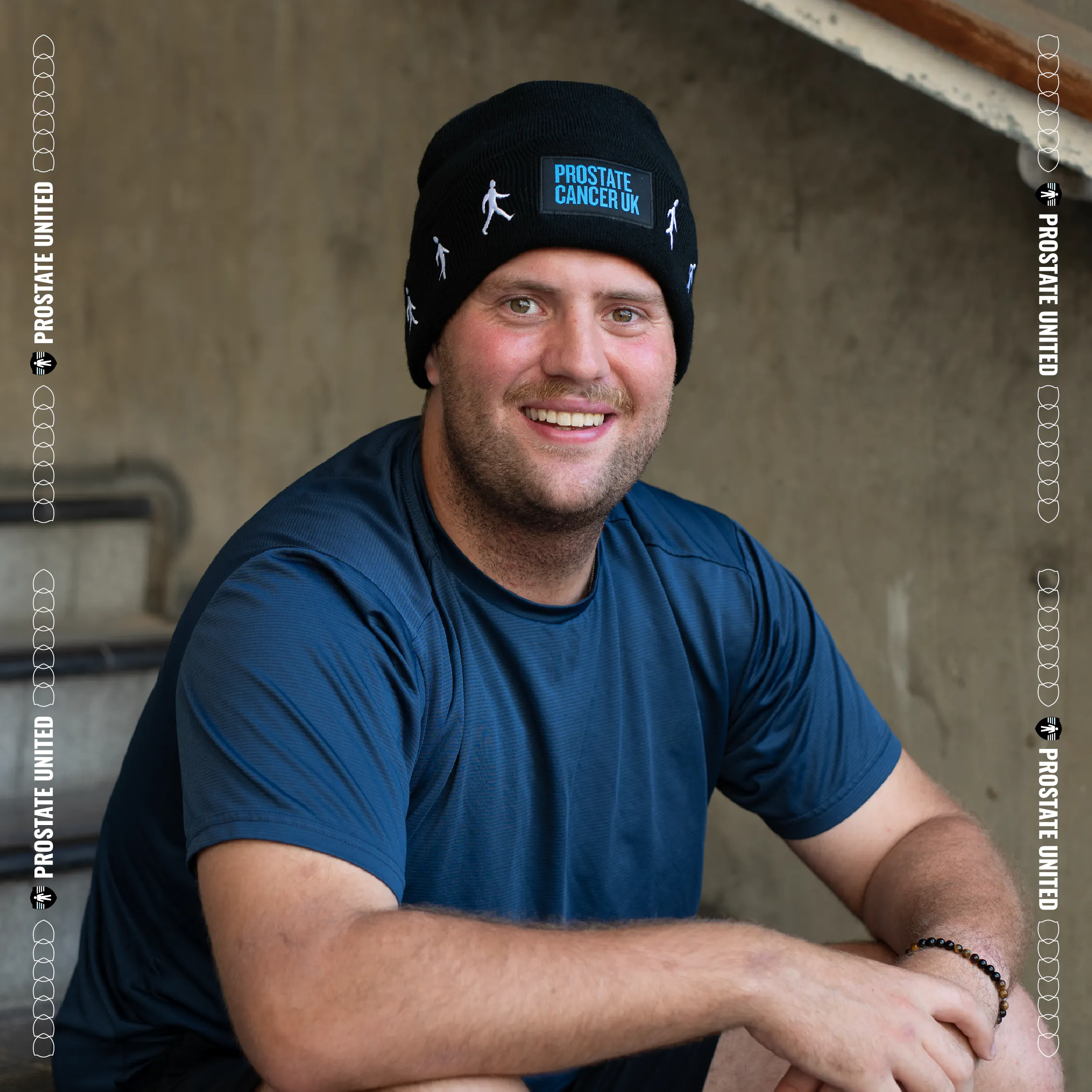 Person wearing a black Prostate Cancer UK branded beanie hat outdoors.