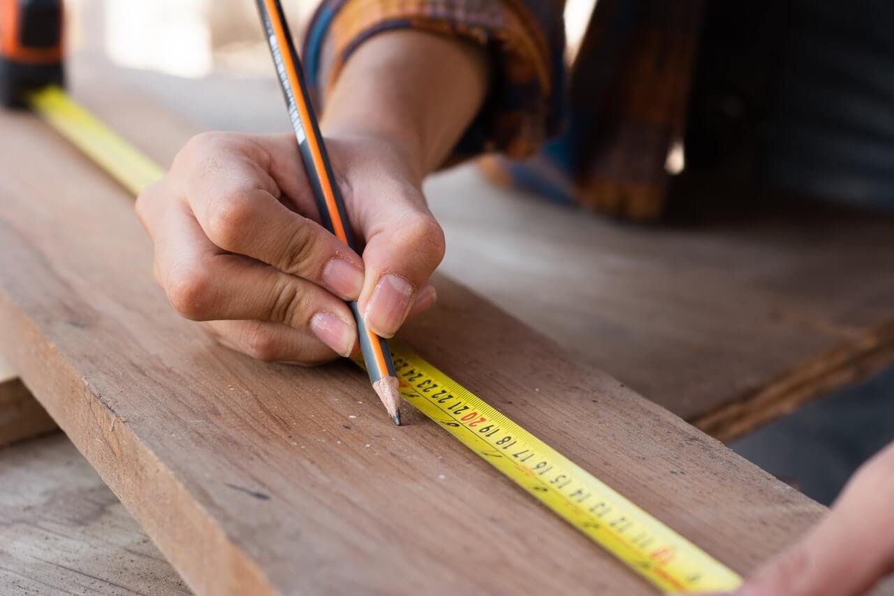 drawing on a piece of wood with a pencil while using a measuring tape