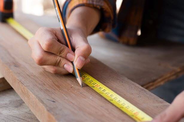 drawing on a piece of wood with a pencil while using a measuring tape