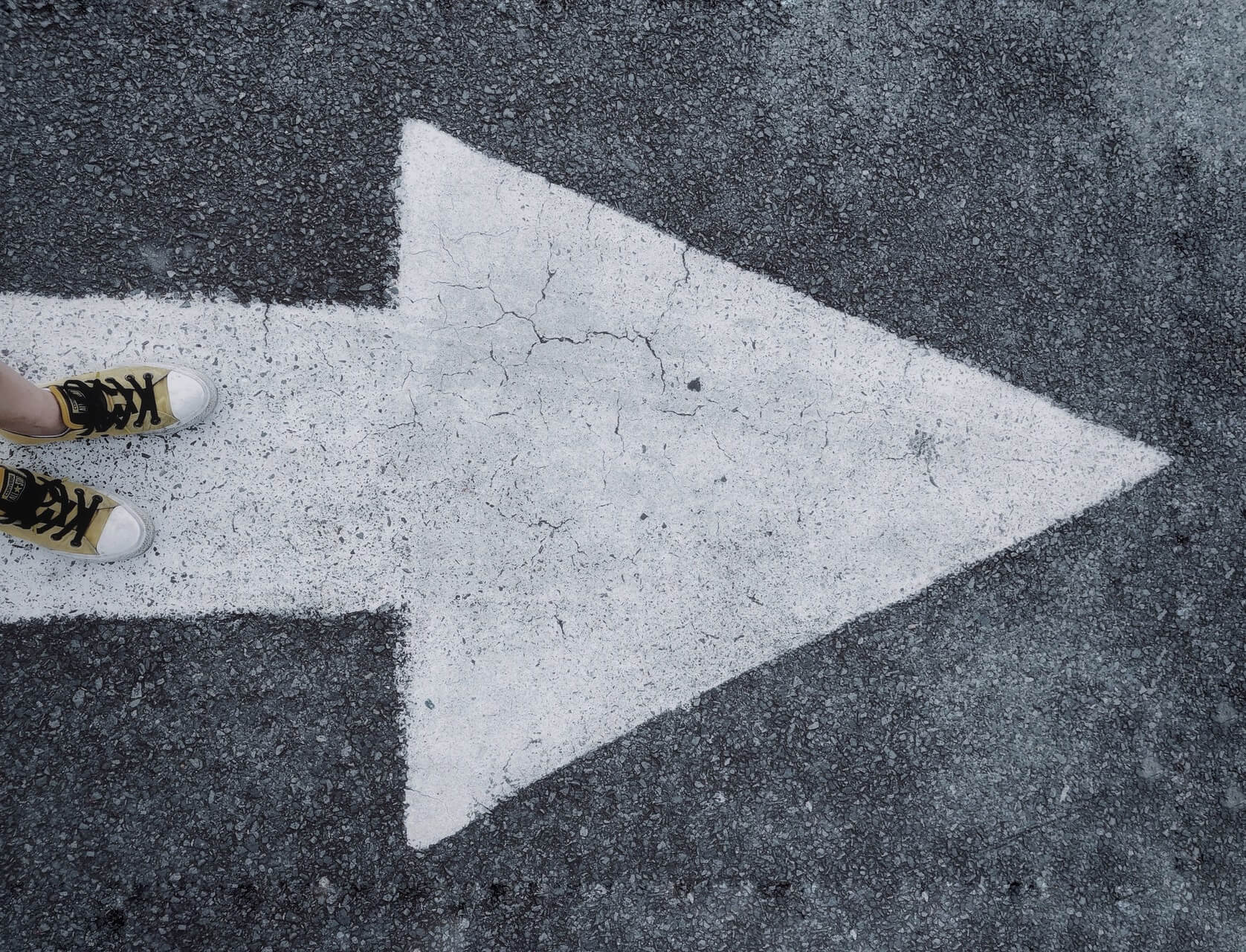 shoes standing on white arrow painted on the ground