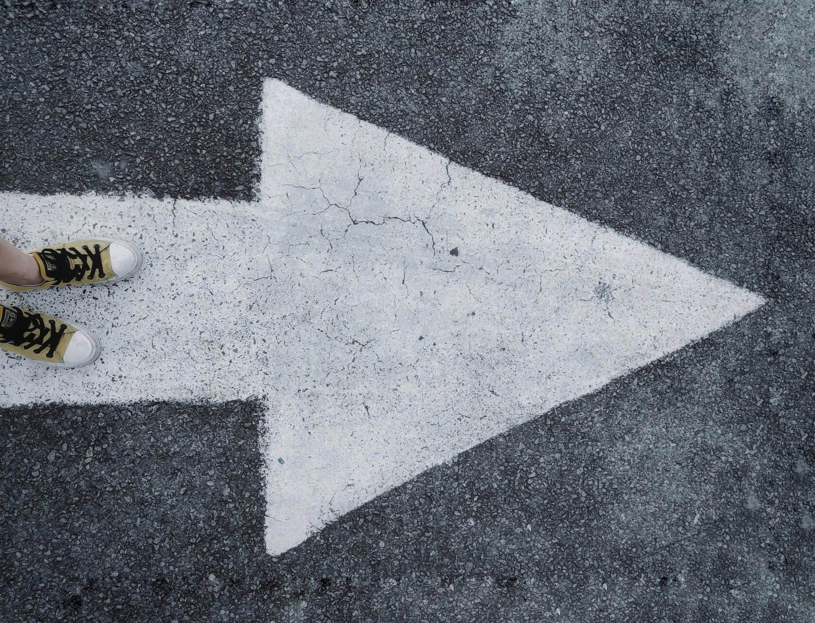 shoes standing on white arrow painted on the ground