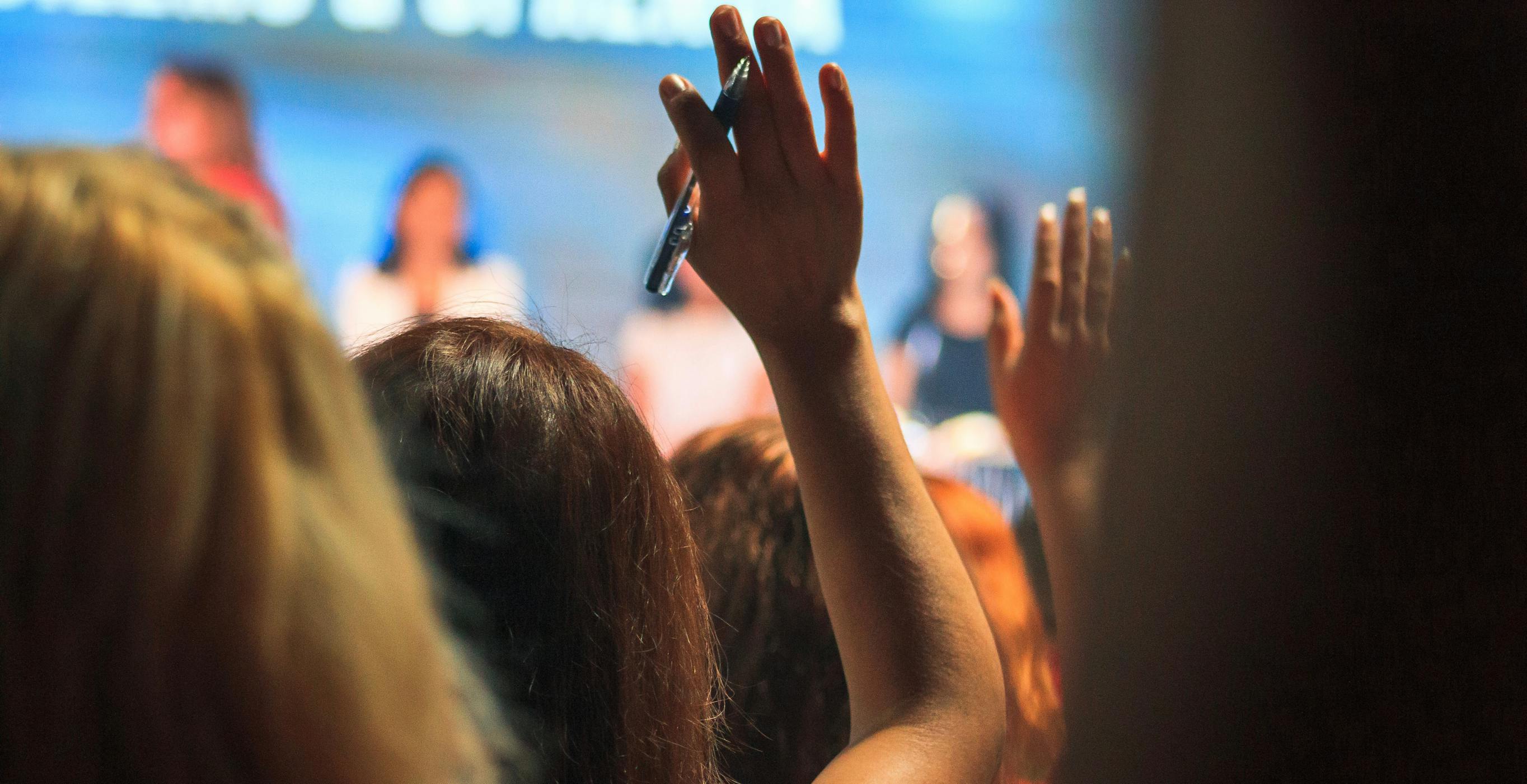 Hands raised at a conference so that the audience can ask questions of the panel