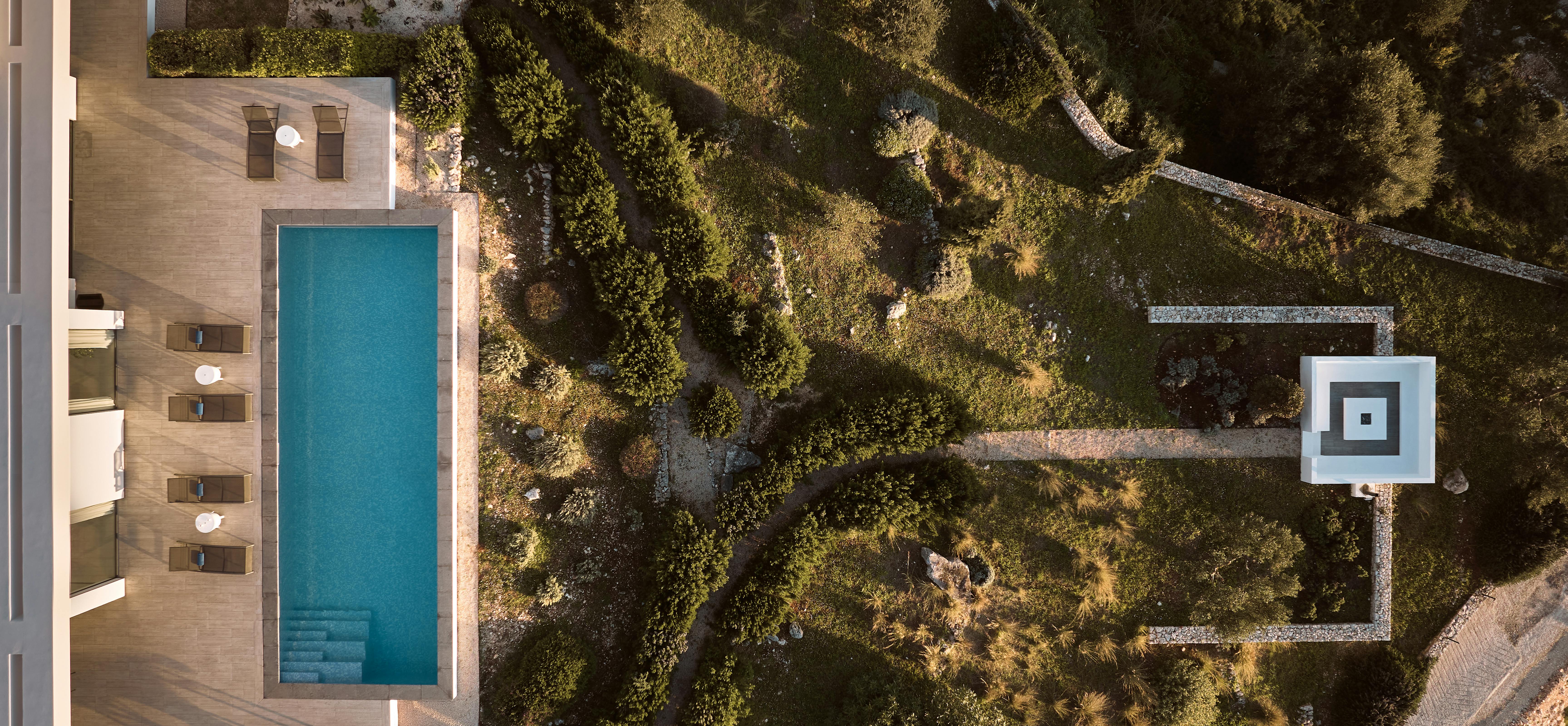 Bird's-eye view of villa grounds showing pool, terraced gardens, winding stone paths, square plunge pool, and native plantings on hillside.