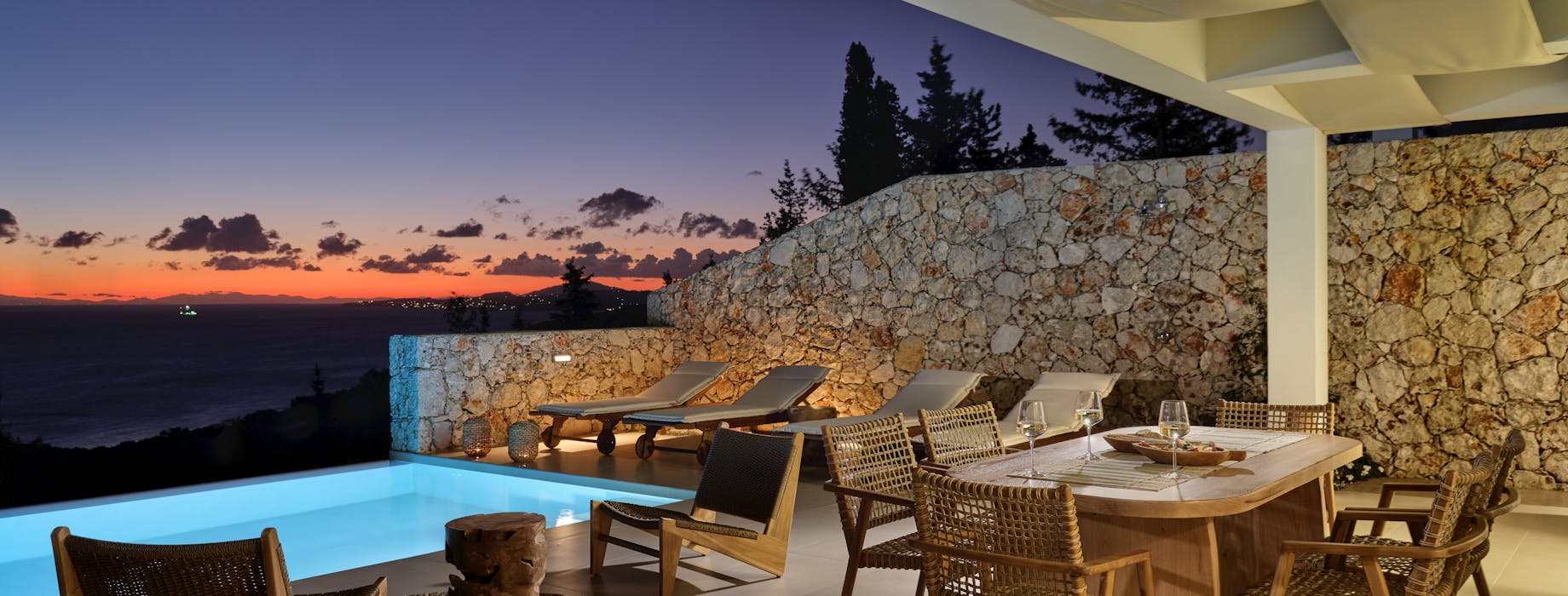 Evening terrace scene with illuminated pool, dining area, and dramatic purple-orange sunset sky.