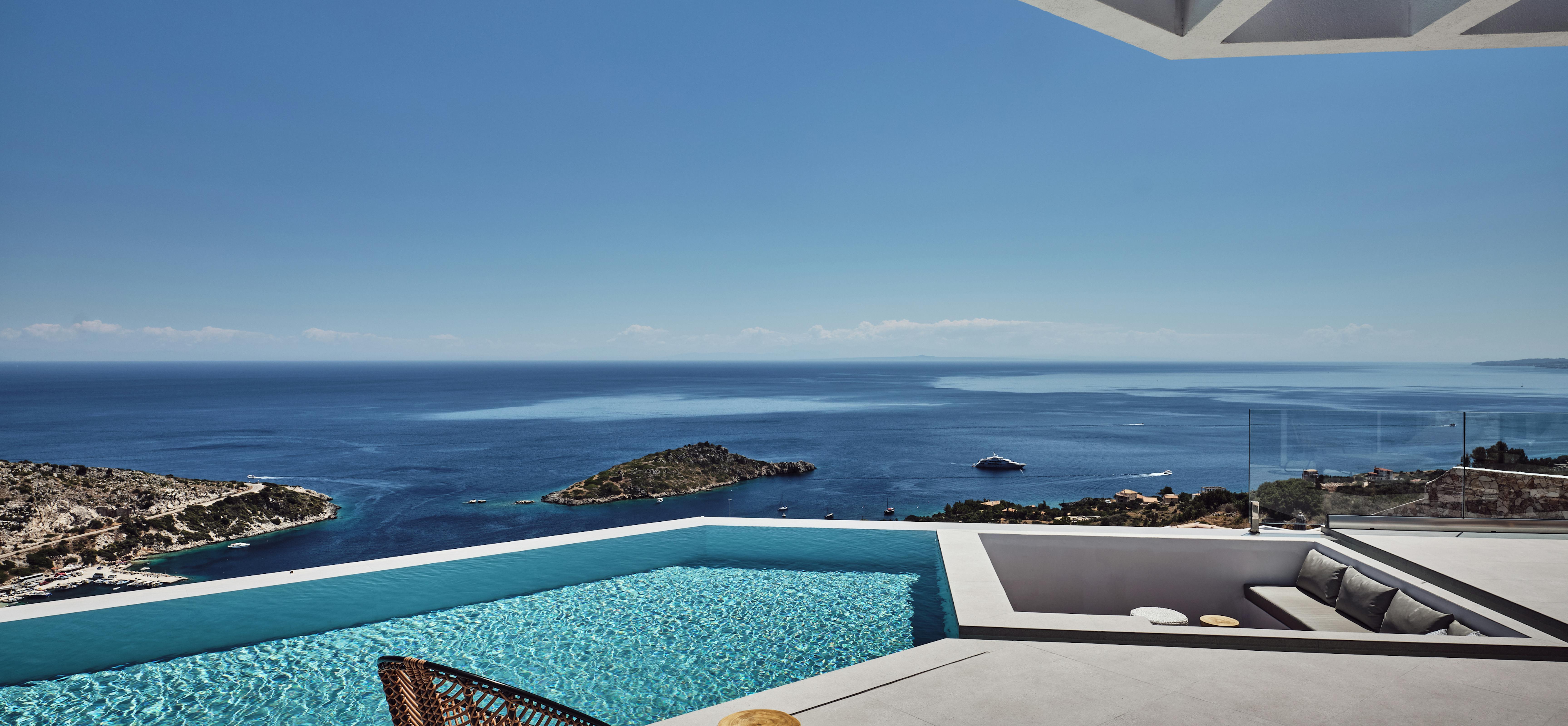 A dramatic infinity pool with modern geometric pergola overlooks coastal islands and deep blue water, with a wicker chair and wooden side table on the minimalist terrace.