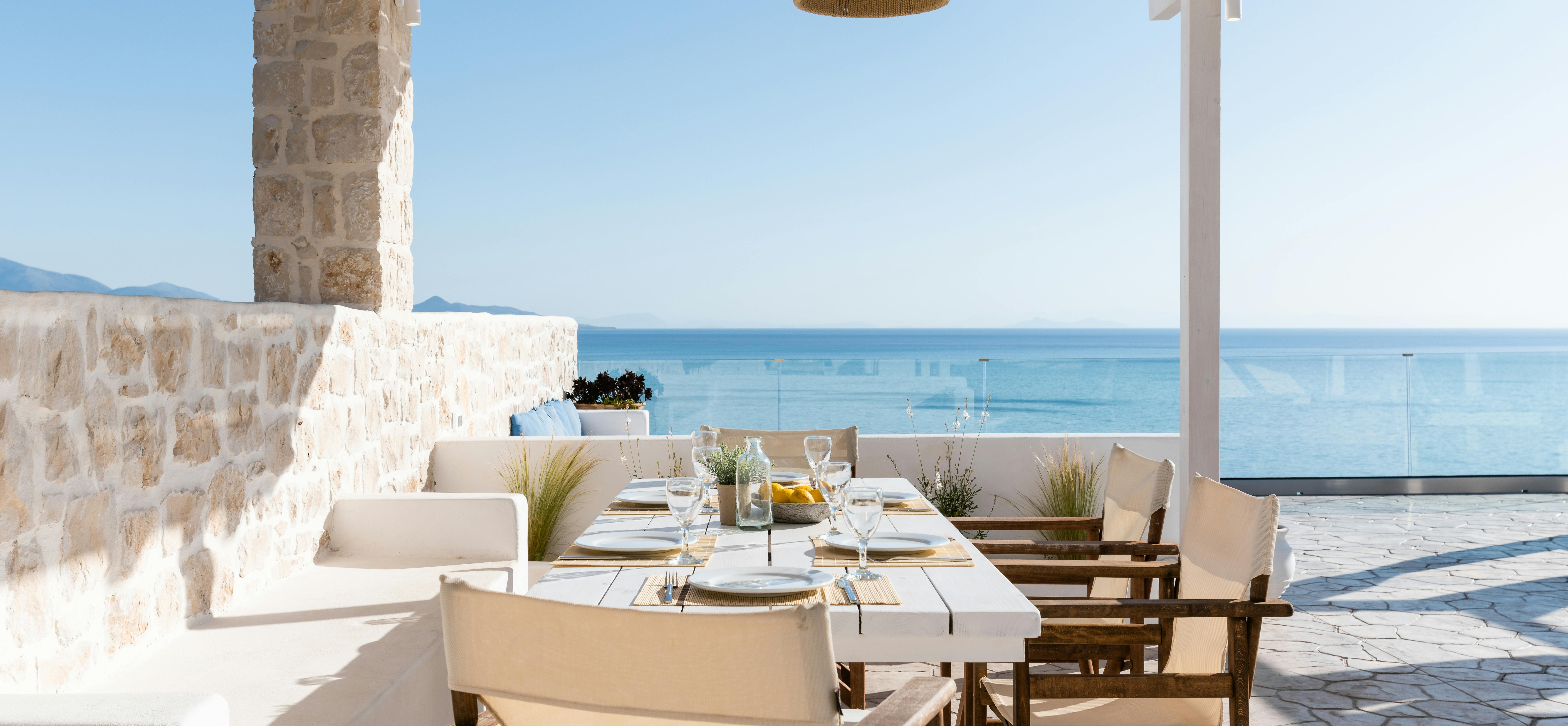 Covered dining terrace with set table, wooden director's chairs, and panoramic ocean views through pergola.