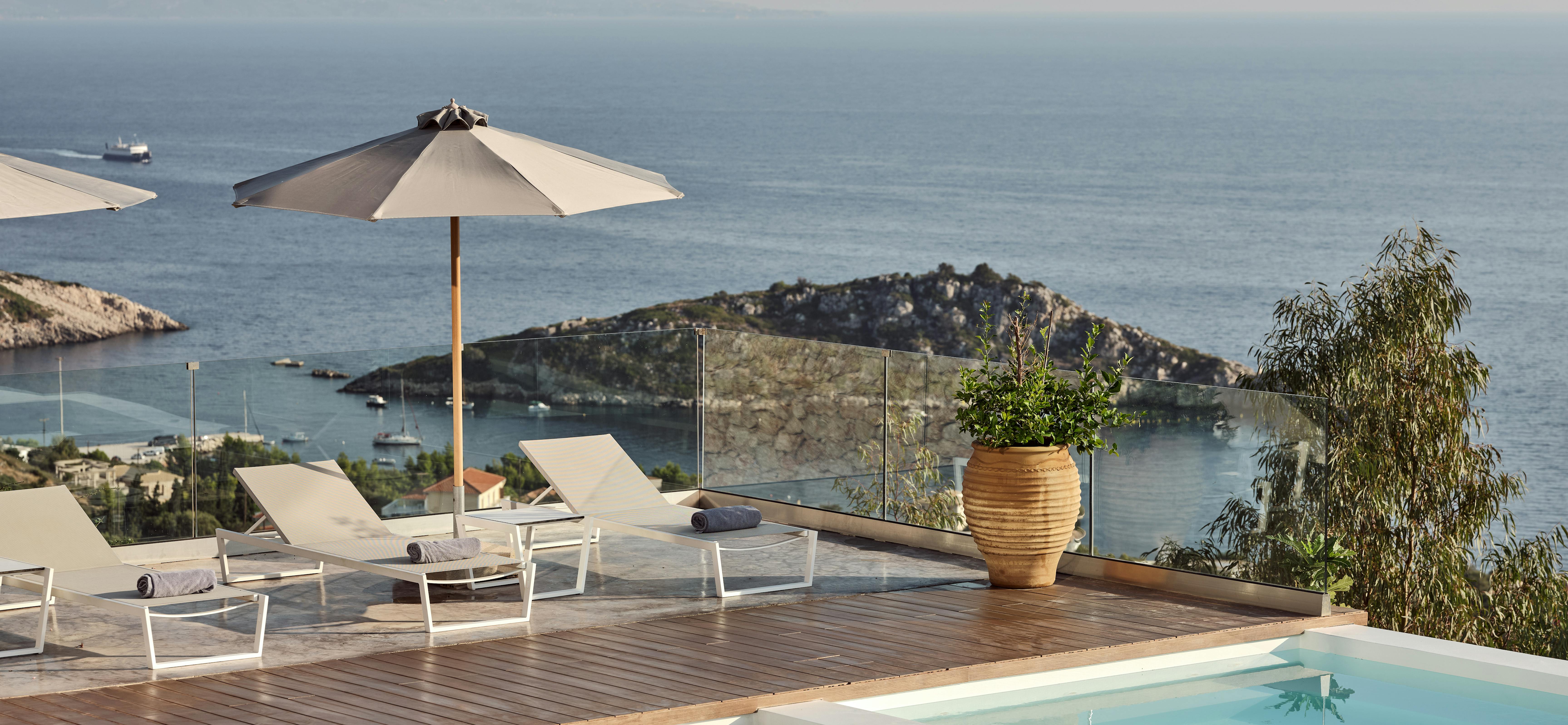 Wooden deck pool terrace with white sun loungers, glass railing, terracotta jar planter, and coastal bay views.