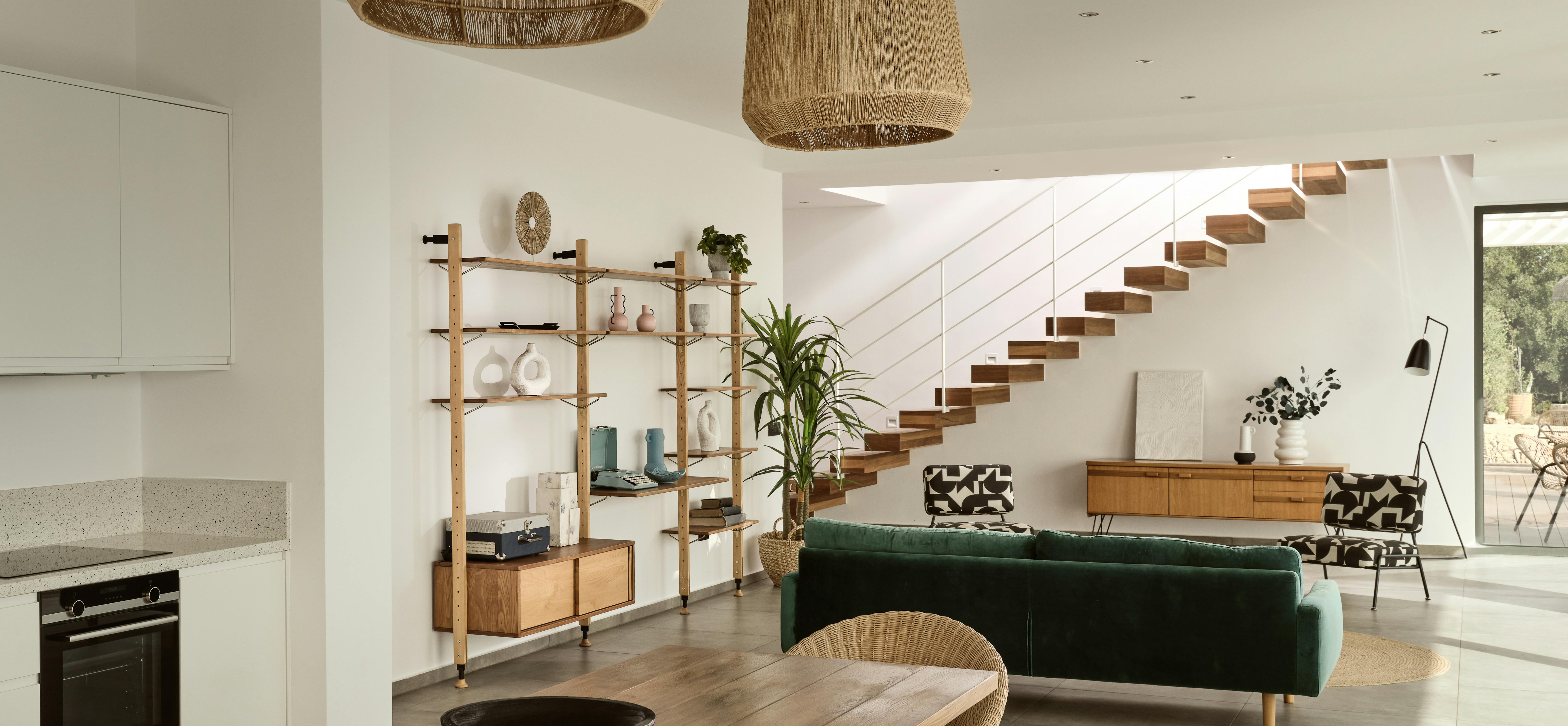Open-plan living and dining area with wooden table, green velvet sofa, floating staircase, and natural pendant lighting.