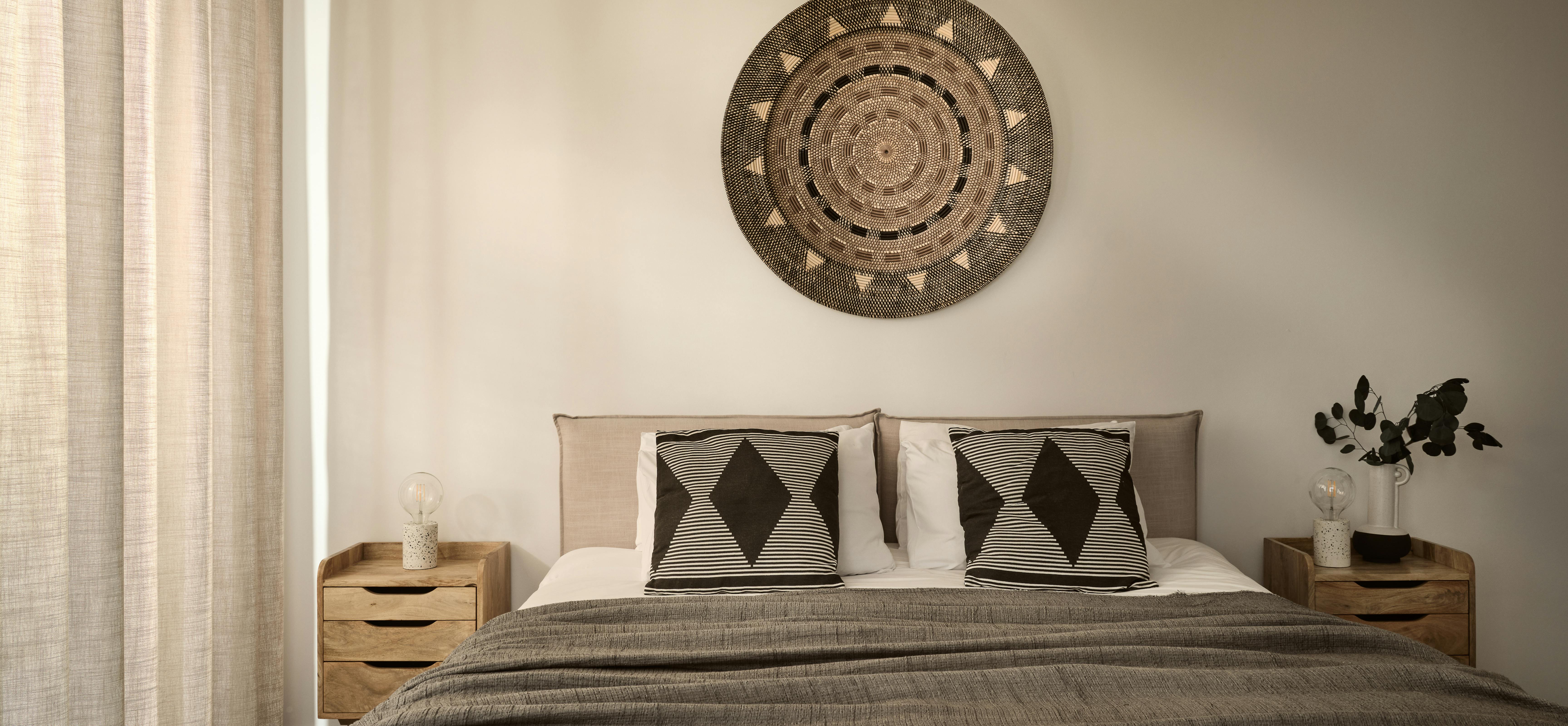 Serene bedroom with circular woven wall art, wooden nightstands, geometric patterned pillows, and textured grey bedding.