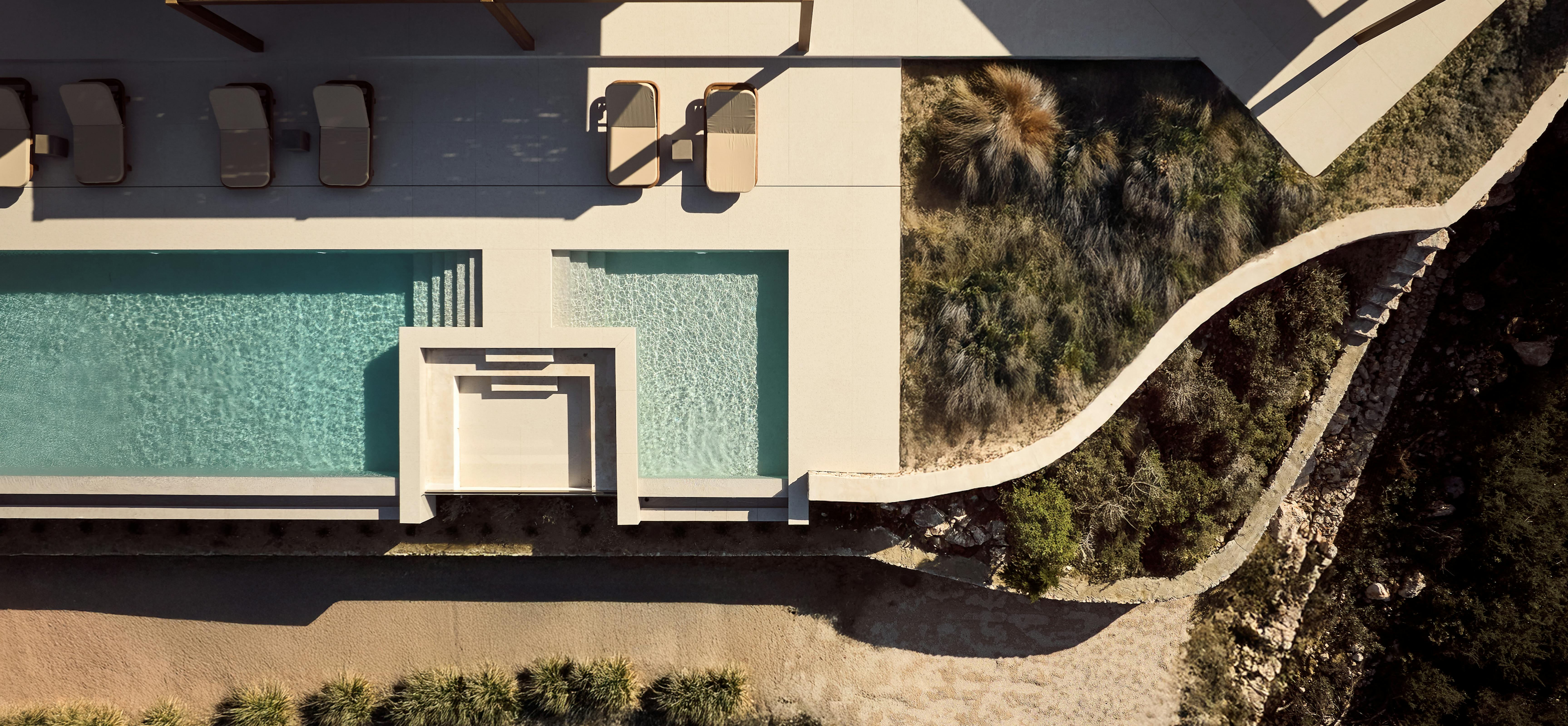 Aerial view of a modern Mediterranean villa with infinity pools, stone terrace, and dramatic coastal landscape with mountain views across the sea.