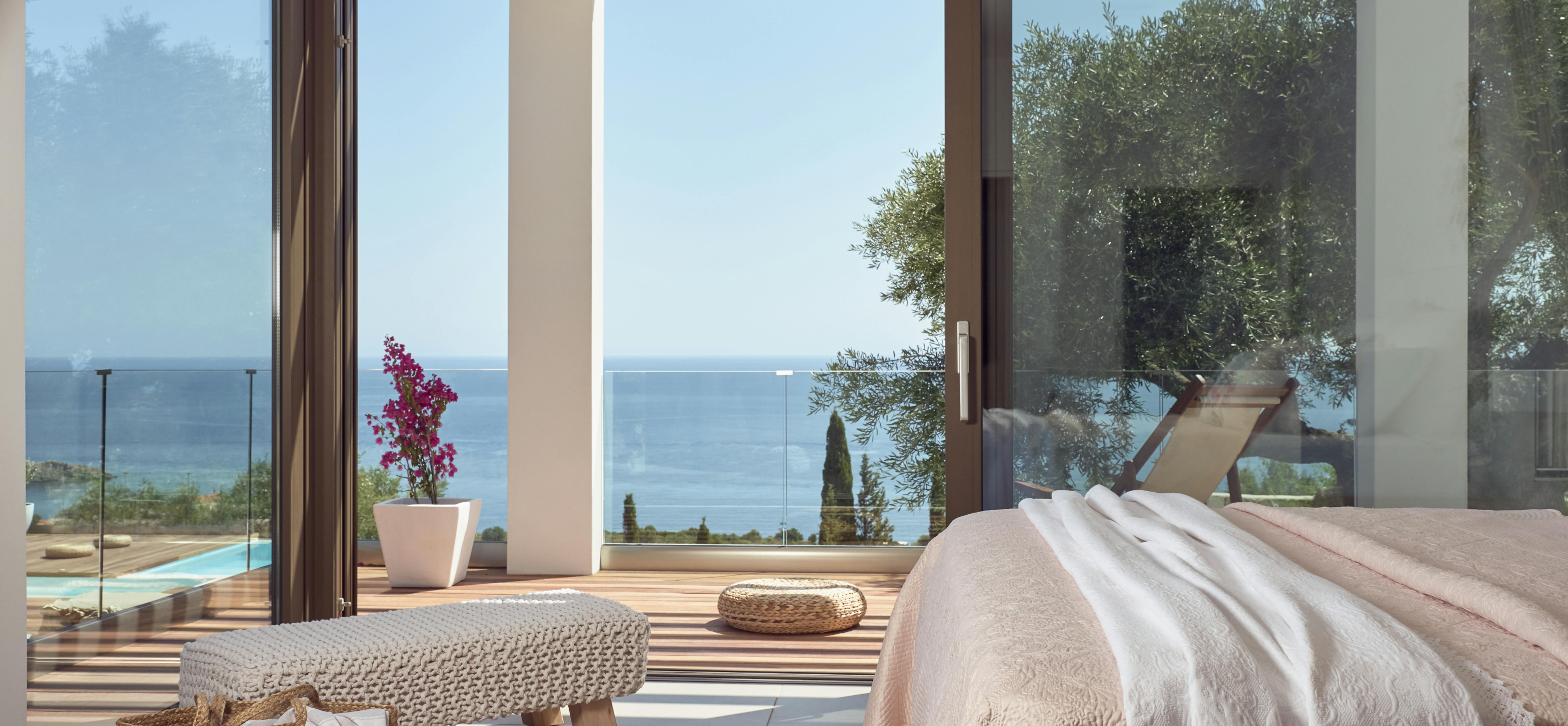 Master bedroom with organic textures opening to wooden deck, infinity pool, and coastal panorama.