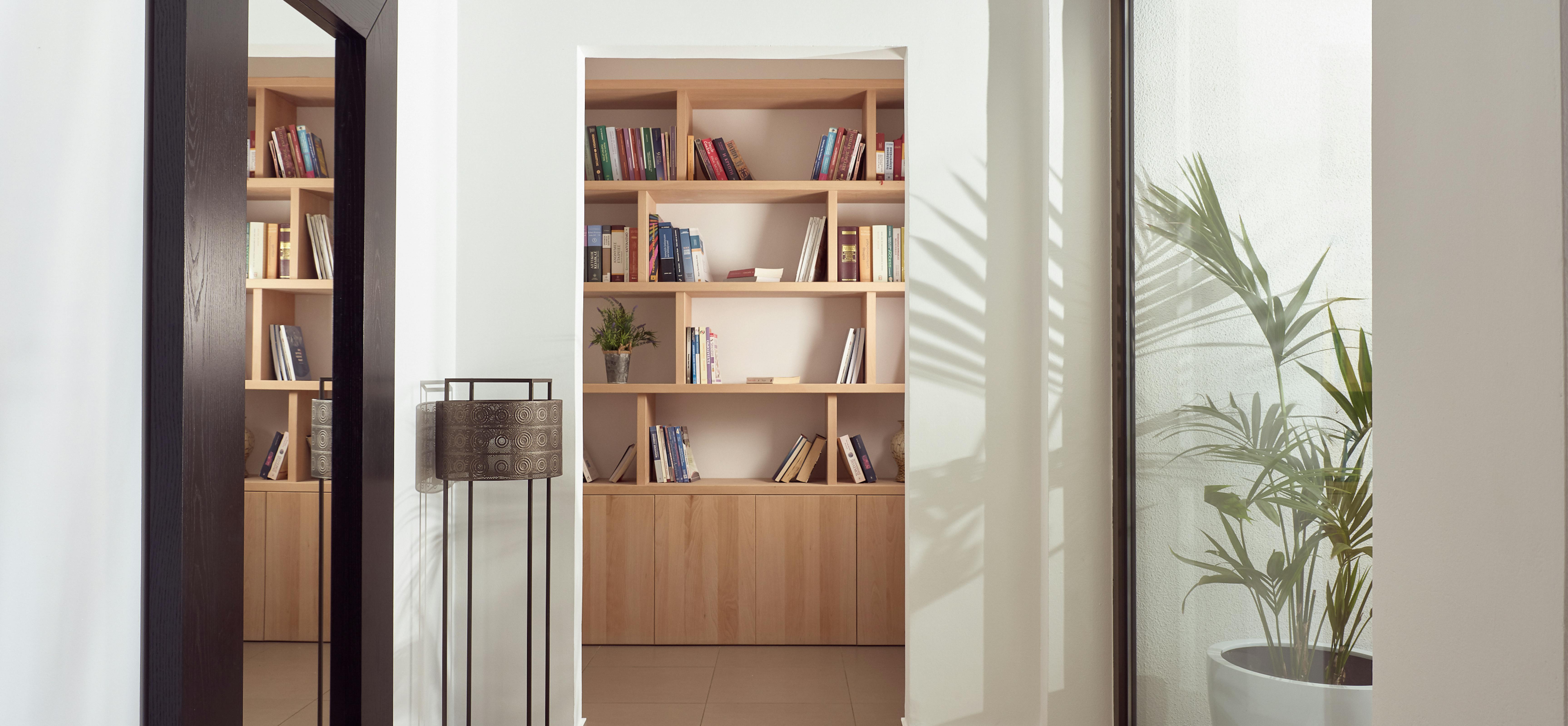 Hallway with built-in wooden bookshelves, contemporary decor, and large windows overlooking gardens.