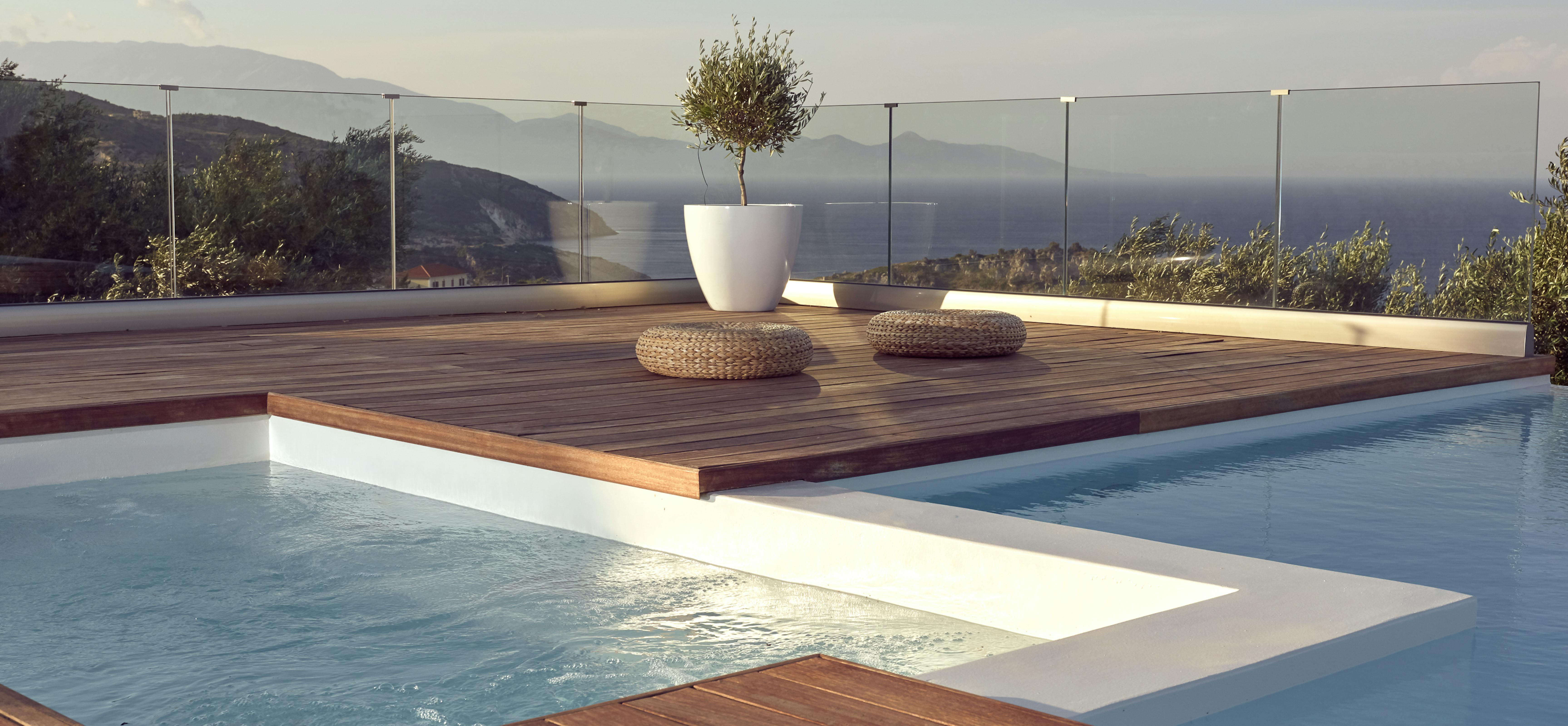 Rooftop terrace with wooden platform surrounded by infinity pool and mountain views beyond glass railings.