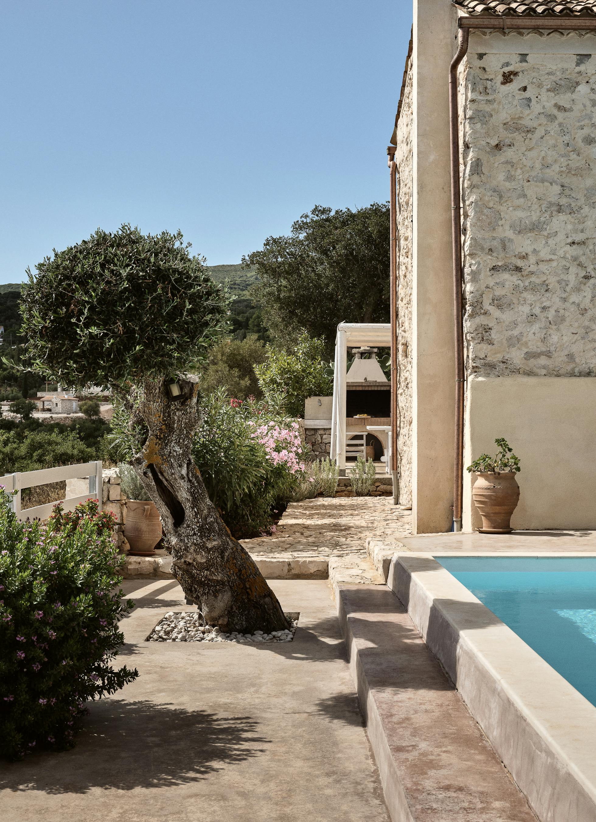 Traditional stone villa with wrought-iron balcony, traditional shutters, and swimming pool nestled in Mediterranean landscape. Ancient olive tree and flowering plants frame this authentic countryside retreat.