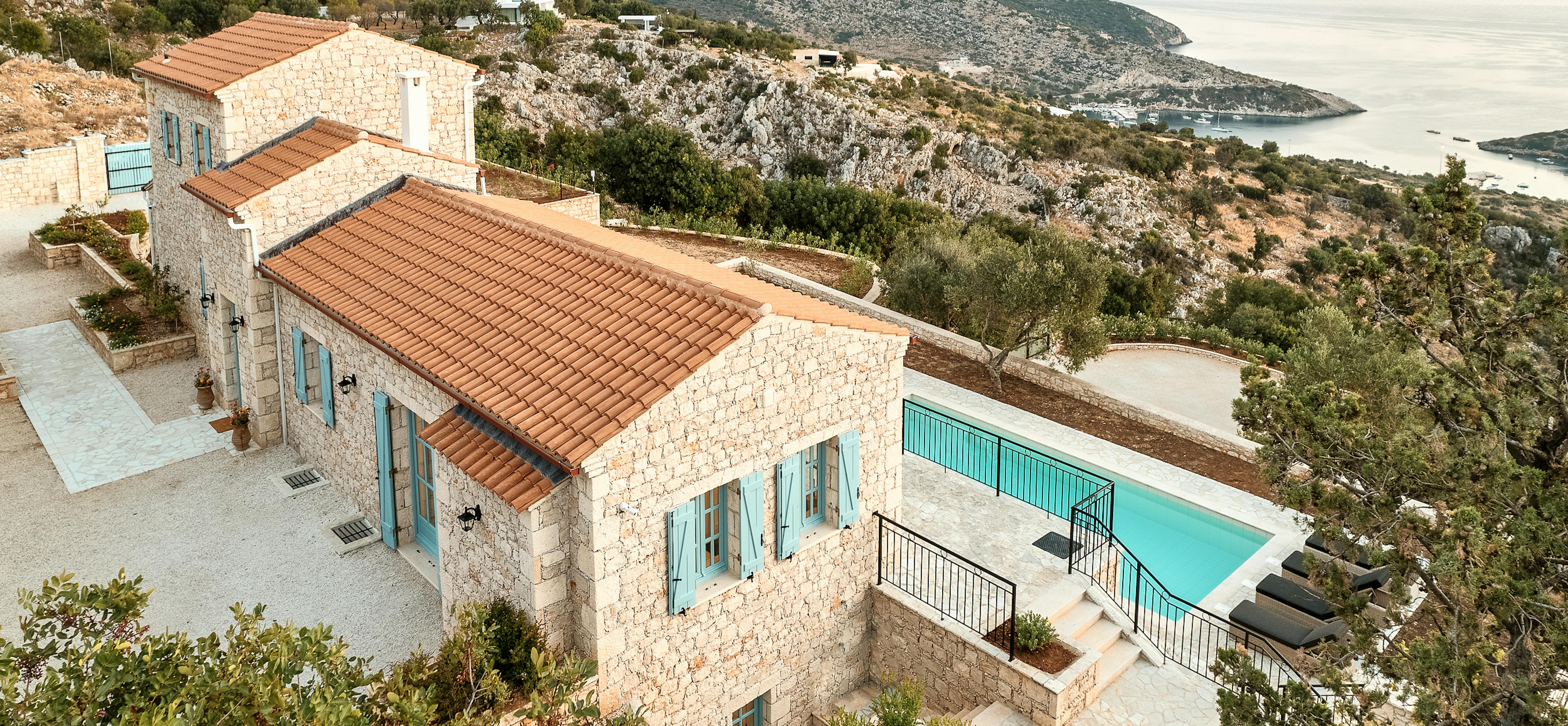Stone villa with terracotta roof overlooking dramatic coastal landscape at golden hour. Traditional architecture harmonises with Mediterranean hillside and distant sea views