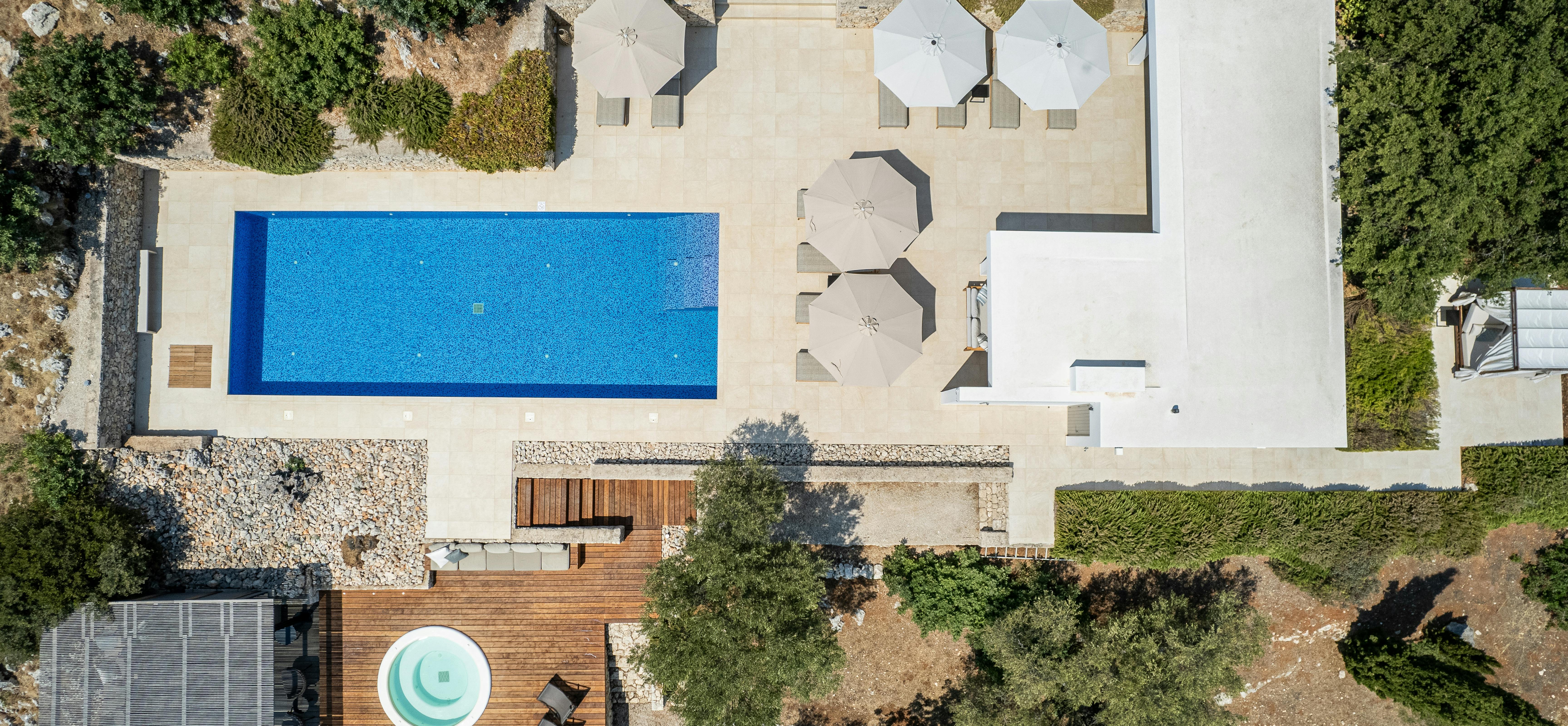 Aerial view of modern villa with rectangular pool, multiple terraces, and wooden hot tub deck.