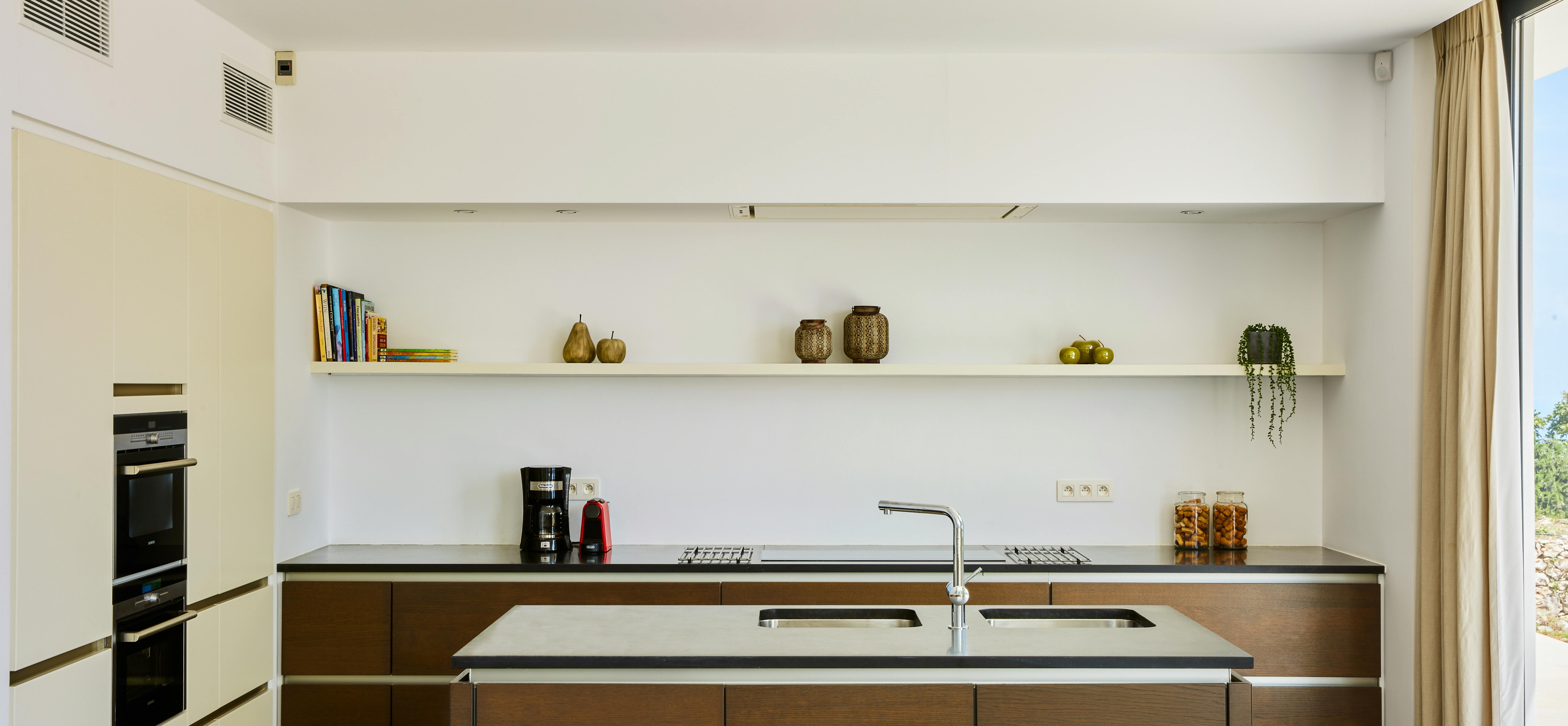 Contemporary kitchen with dark wood cabinets, white countertops, and floating shelves displaying decorative items.
