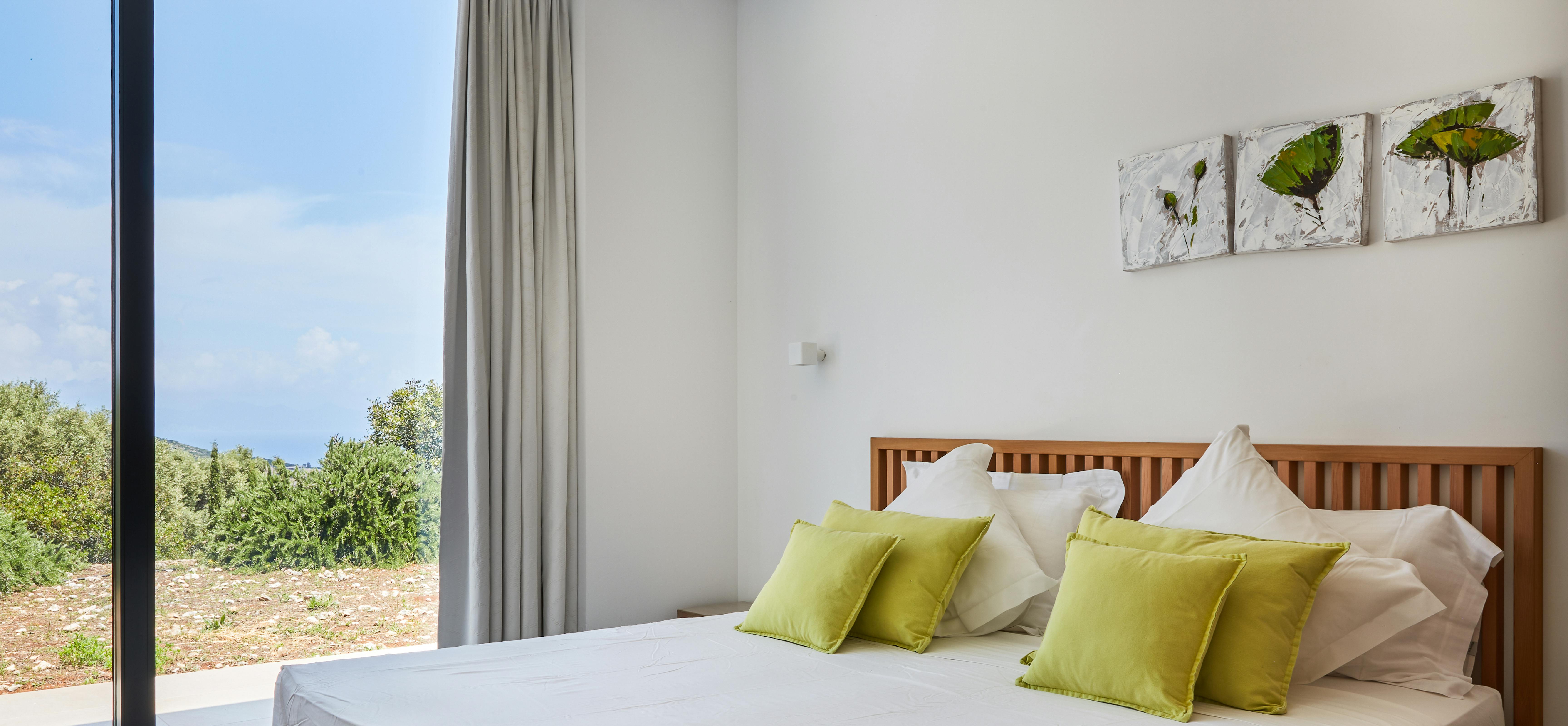 Bedroom featuring wooden slat headboard, green throw pillows, and botanical artwork on white walls.