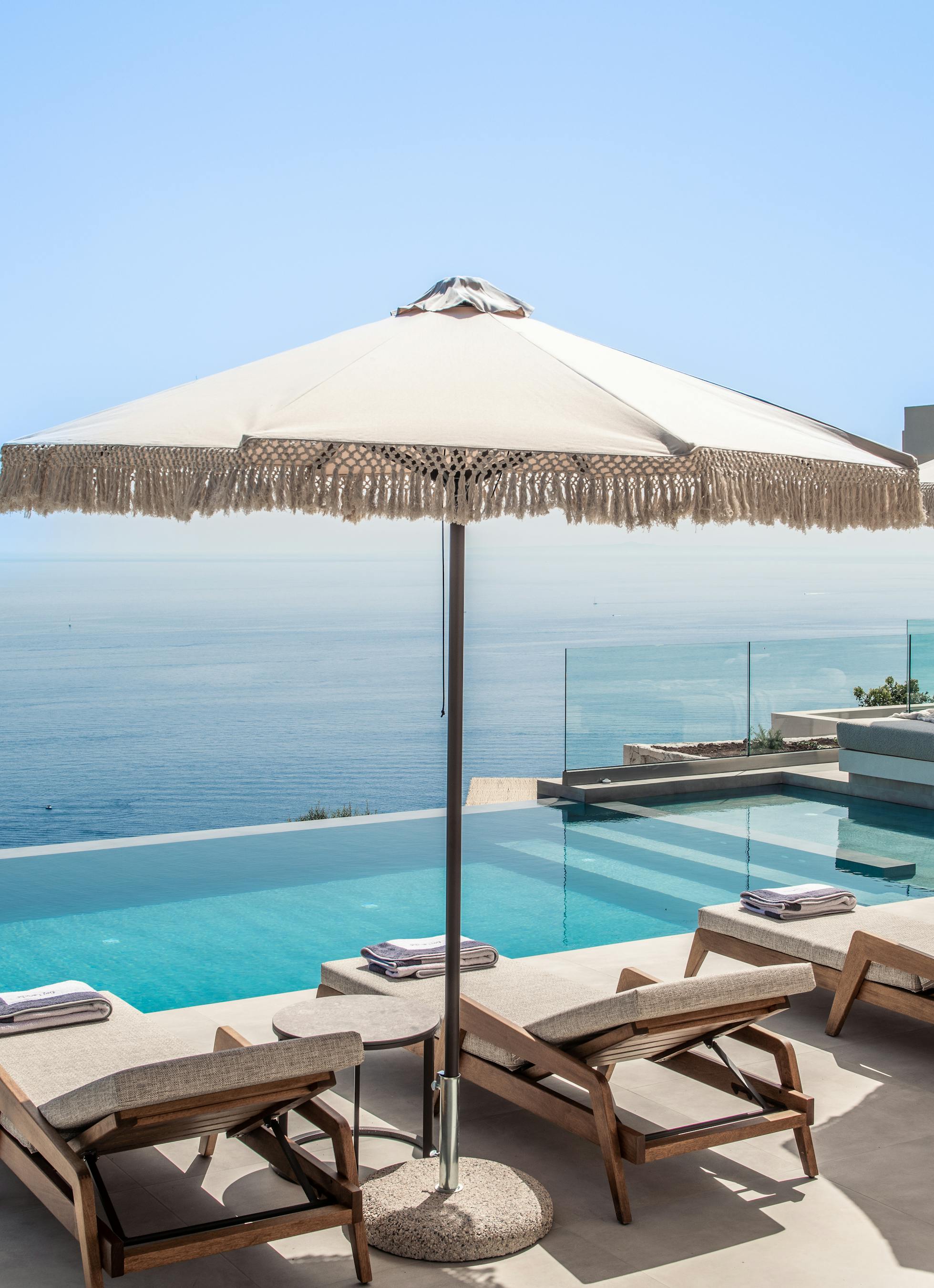 Infinity pool deck with wooden loungers, fringed umbrella, and dramatic ocean horizon views.