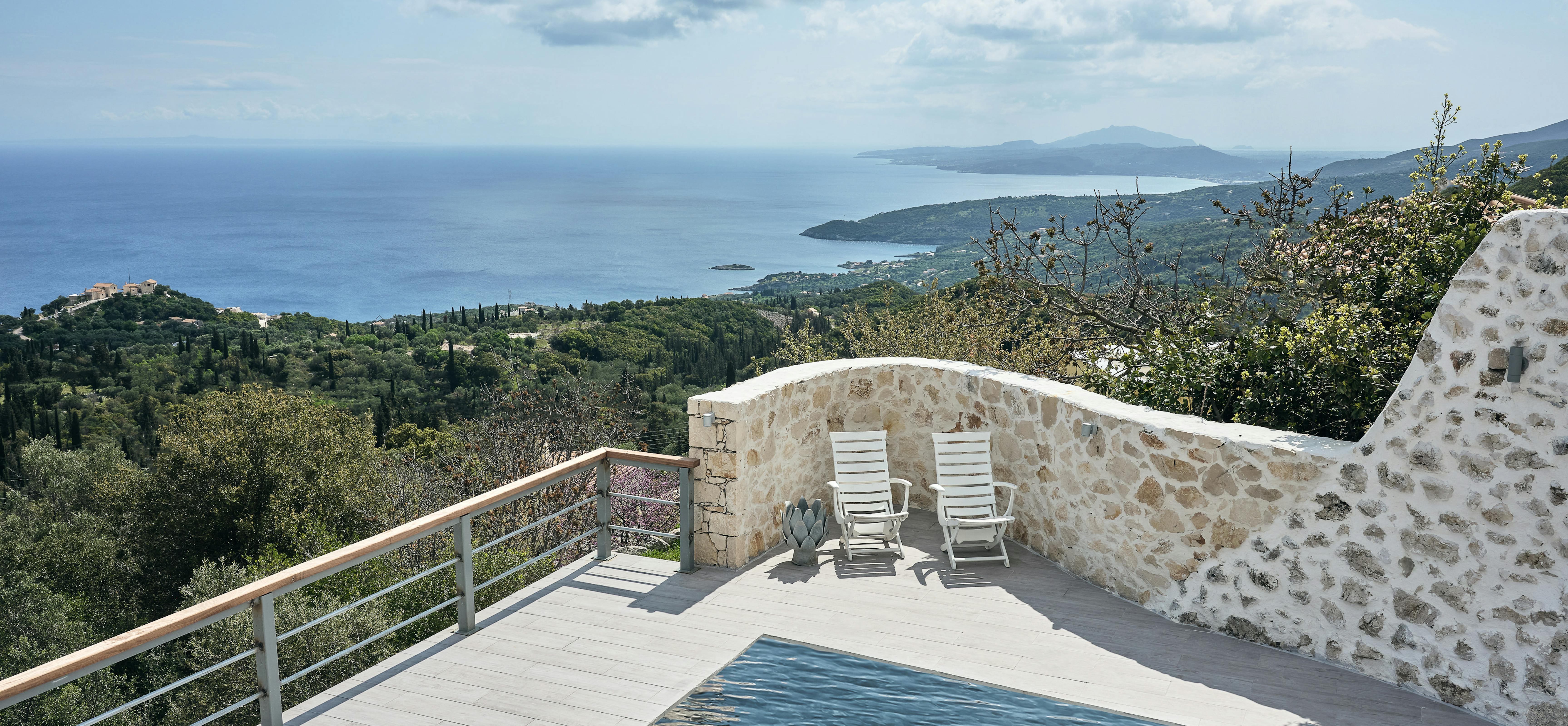 A curved infinity pool overlooks the Mediterranean coastline with white sun loungers positioned for optimal sea views. The clifftop terrace is enclosed by natural stone walls with the azure sea stretching to the horizon.