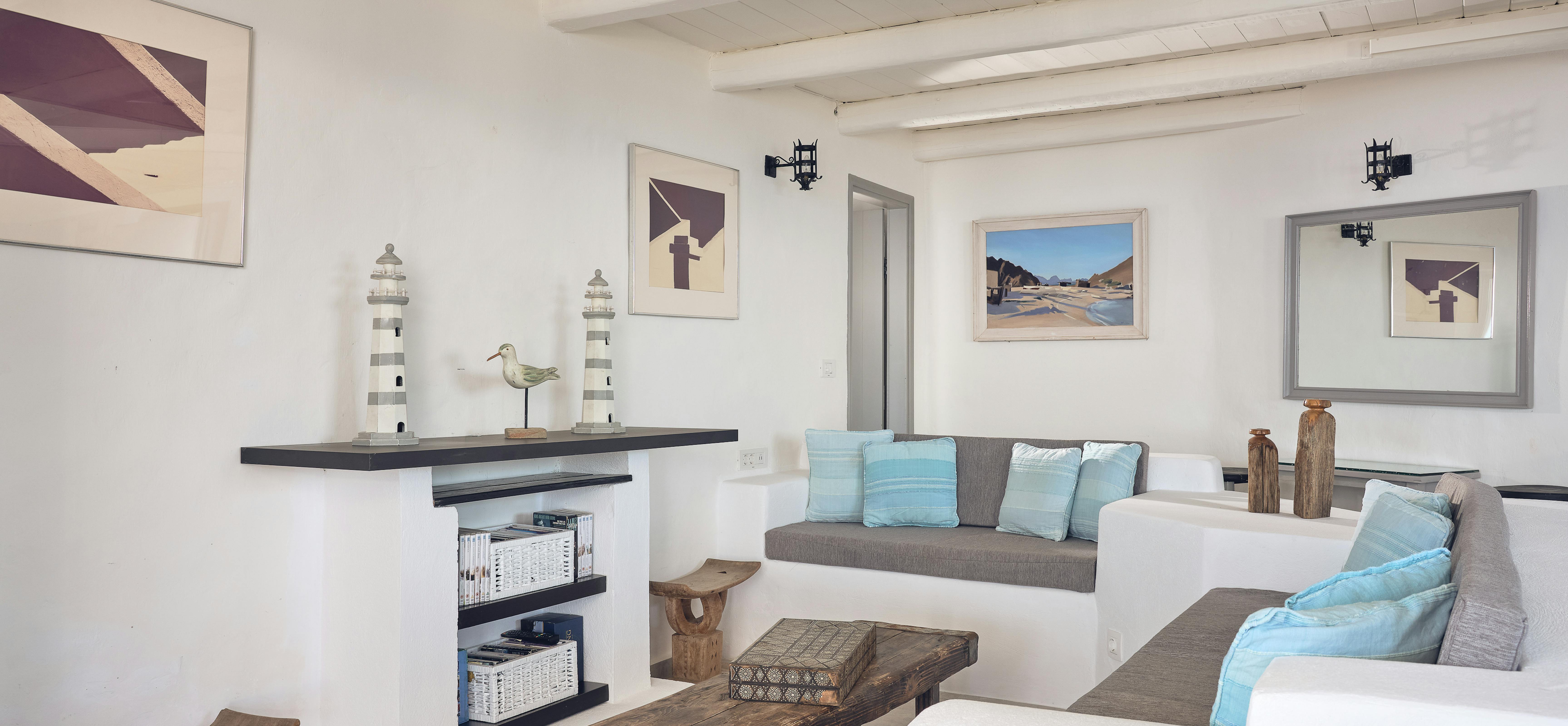 Built-in white seating with turquoise cushions creates a nautical-themed lounge area beneath exposed ceiling beams. The coastal-inspired space includes lighthouse decorations, weathered timber furniture, and framed maritime artwork.